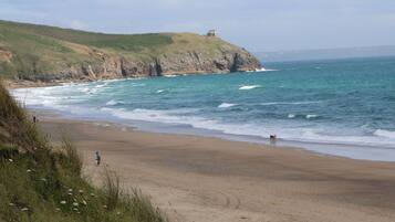 A coastal beach with a rocky cliff and a lighthouse.