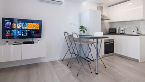 A modern kitchen with white cabinets, a dining area with a foldable table and chairs, a flat-screen TV mounted on the wall, and an air conditioning unit above the counter. - BUNGALOW CAMPO DE GOLF (San Bartolomé de Tirajana)