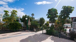 A courtyard with tiled flooring, a green fence, and various tropical plants. - BUNGALOW CAMPO DE GOLF (San Bartolomé de Tirajana)