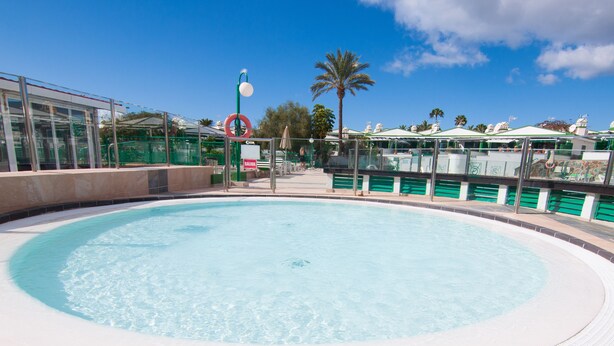 A circular pool with a textured edge, surrounded by a low wall and a glass barrier. - BUNGALOW CAMPO DE GOLF (San Bartolomé de Tirajana)