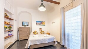 Ein Schlafzimmer mit einem Bett, einem Schminktisch, Regalen mit Pflanzen, einem Gemälde und einem Fenster mit Vorhängen.