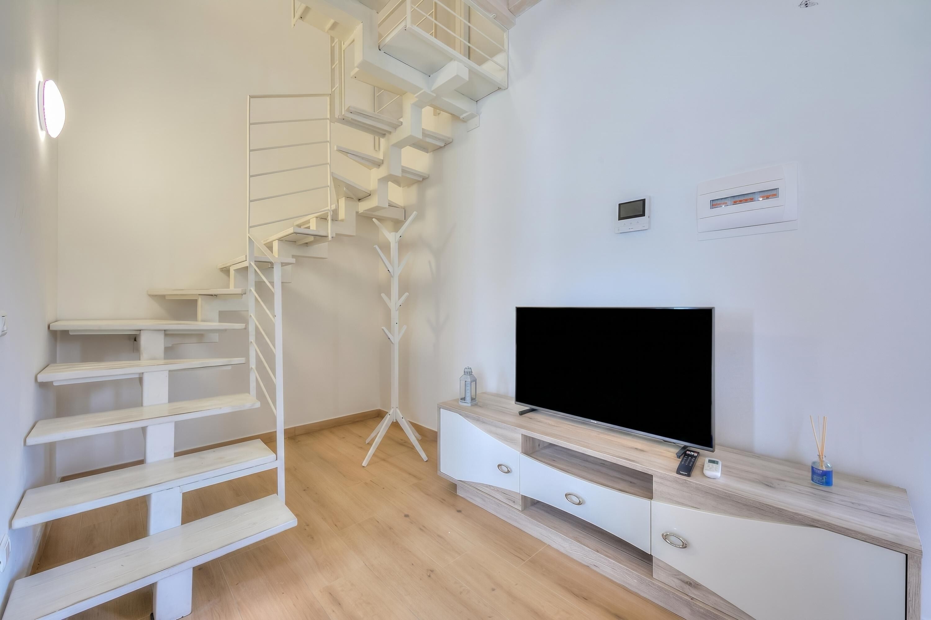 A modern living room with a white staircase, a flat-screen TV, and a minimalist wooden entertainment unit.