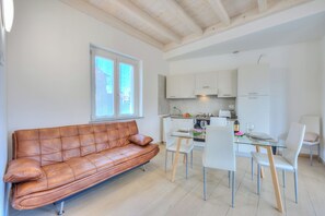 A modern kitchen with white cabinets, a dining table with chairs, and a brown leather sofa.