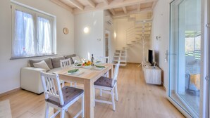 Ein moderner Essbereich mit einem Holztisch, weißen Stühlen und einer Couch. Eine Treppe führt zu einer erhöhten Ebene.