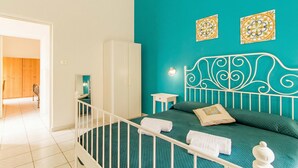 A bedroom with a teal wall, a white metal headboard, a bed with green bedding, a white wardrobe, and two decorative wall pieces. - Sicula home in the city center (Catania)
