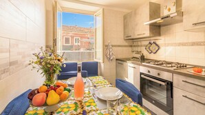 A kitchen with a dining table set for two, a gas stove, oven, and a window with a view of buildings. - Sicula home in the city center (Catania)