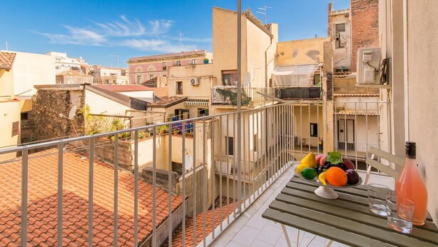 A balcony with a metal railing, a table with a fruit bowl, a bottle, and a glass. - Sicula home in the city center (Catania)