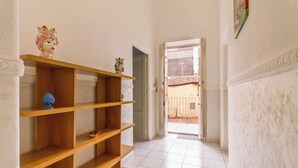 A hallway with wooden shelves, a white wall with a decorative molding, and a door leading to an outdoor area. - Sicula home in the city center (Catania)