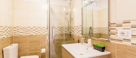 A modern bathroom with a glass-enclosed shower, a toilet, and a sink with a mirror.