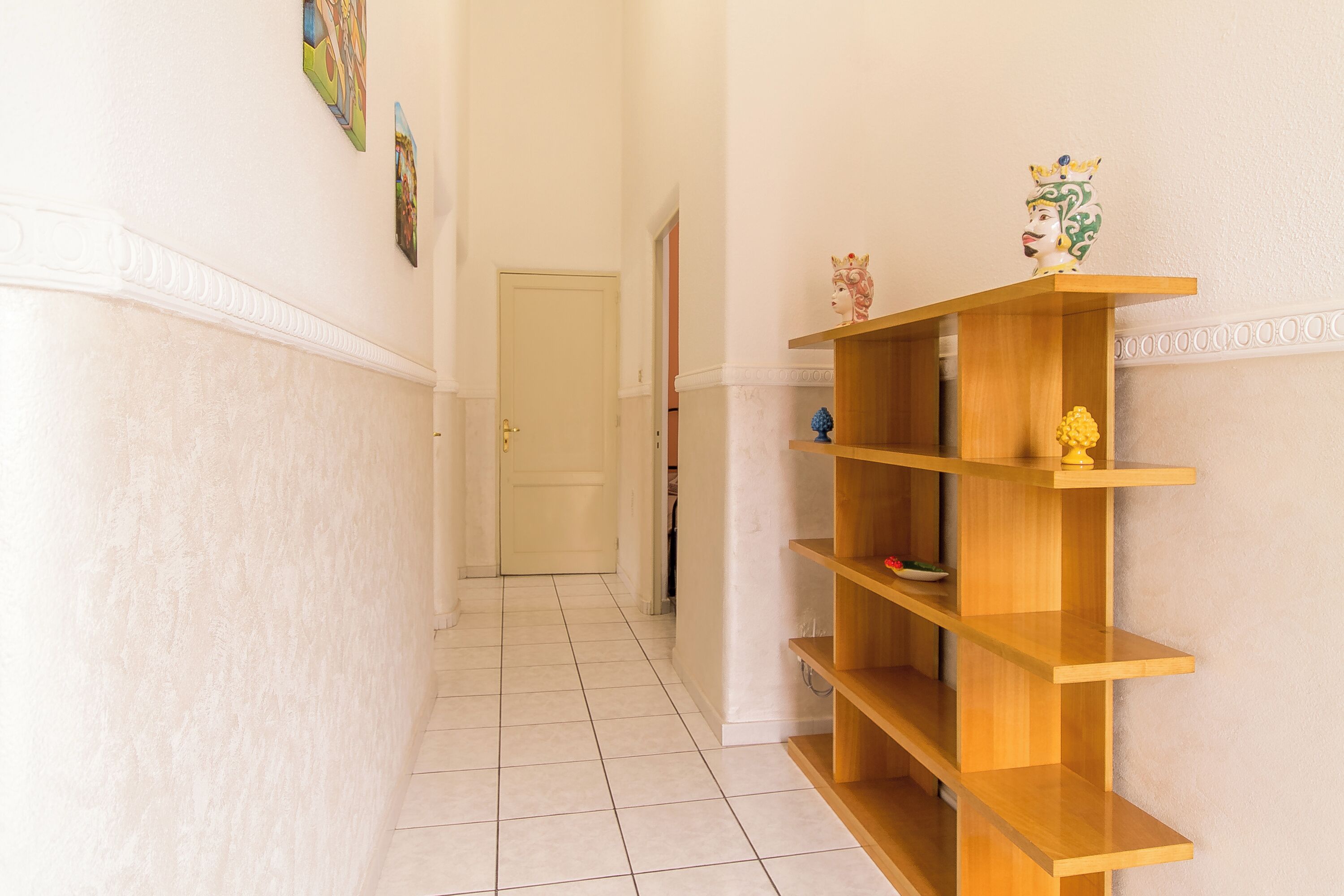 A hallway with a wooden bookshelf, a door, and a tiled floor.