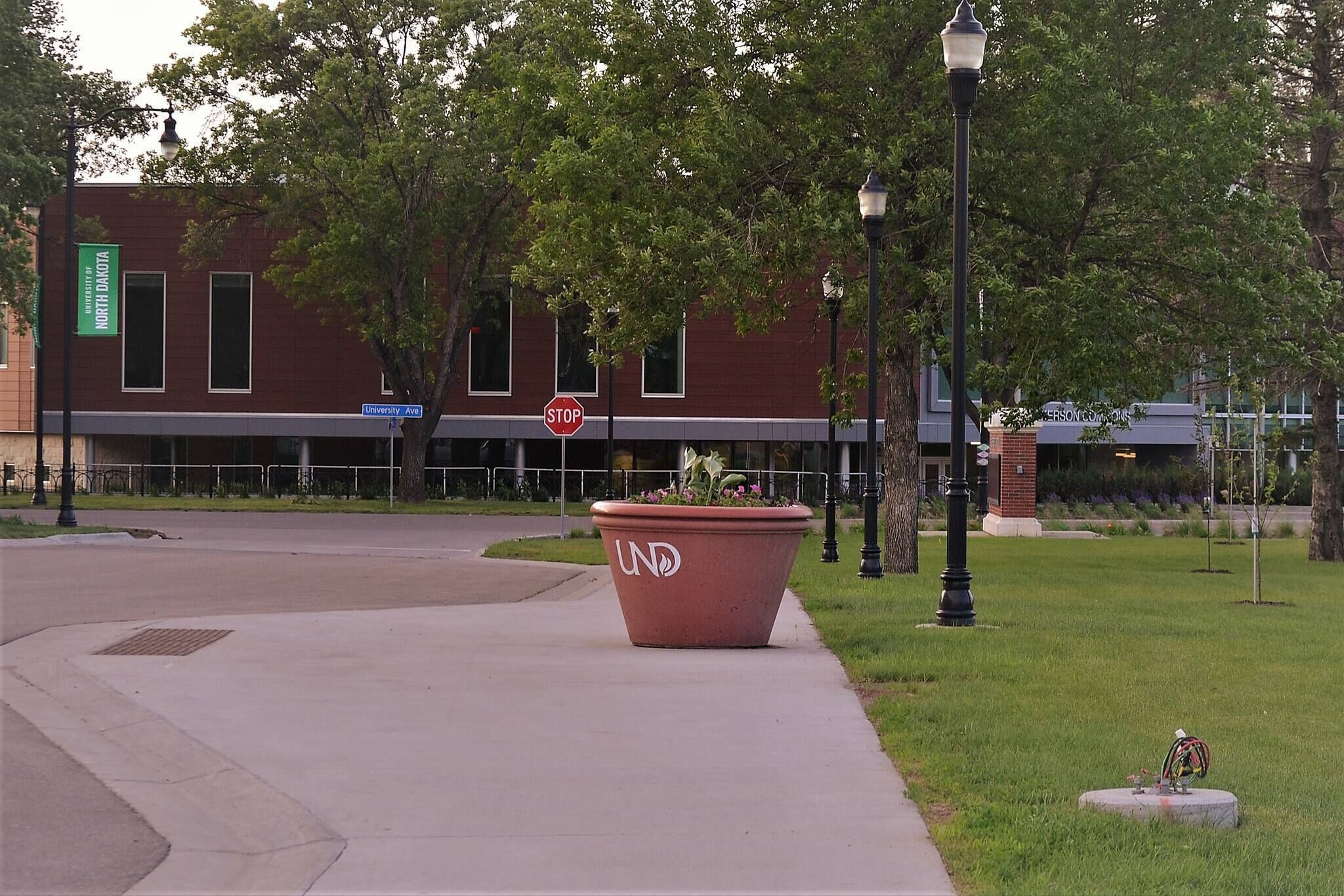 A campus building with a stop sign, a large planter with flowers, and a lamp post.
