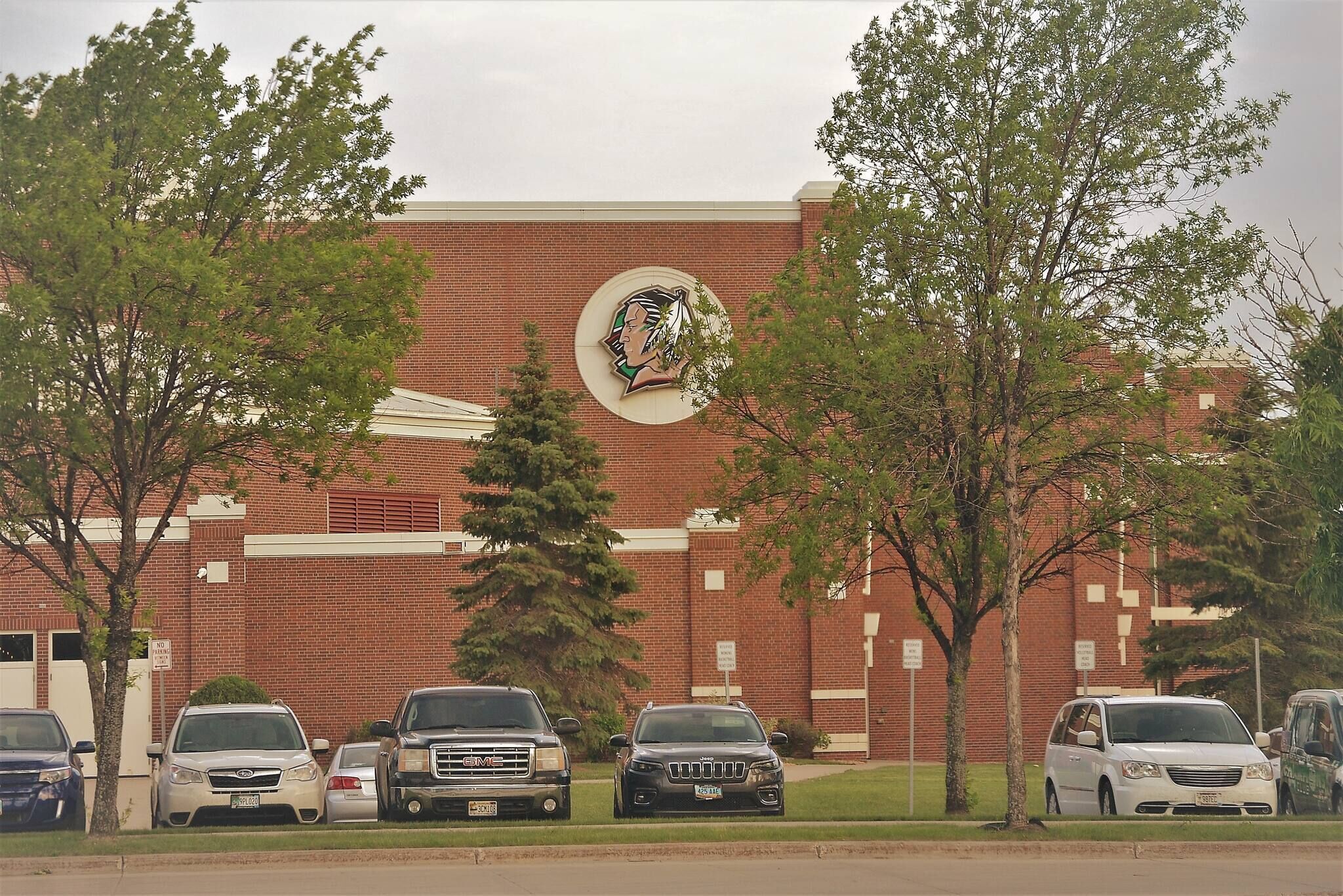 Un bâtiment avec un grand logo sur la façade, entouré de voitures garées et d’arbres.