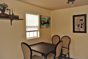 A dining area with a table and four chairs, a window with blinds, and wall art.