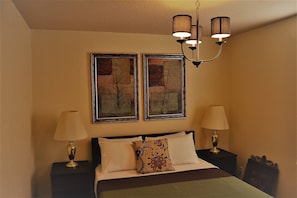 A bedroom with a bed, two bedside lamps, a chandelier, and two framed pictures on the wall. - The Gateway - a Beautiful Relaxing Three Bedrooms Apartment (Grand Forks)