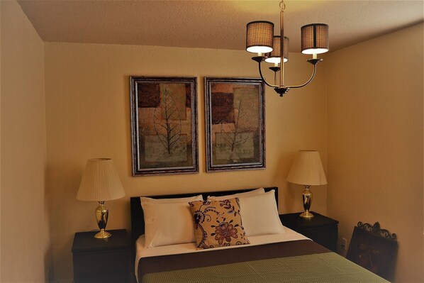 A bedroom with a bed, two bedside lamps, a chandelier, and two framed pictures on the wall.