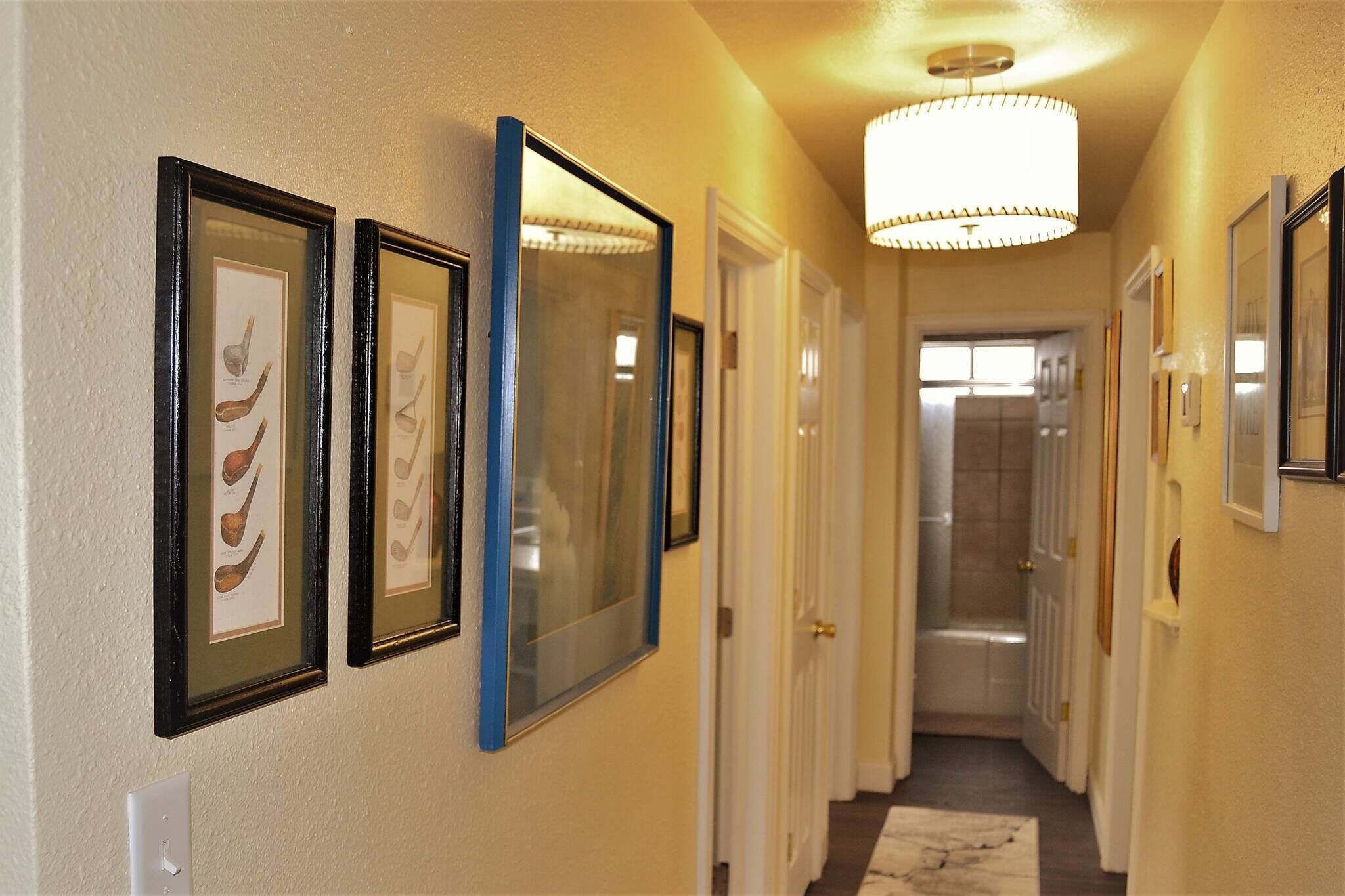 A hallway with framed artwork, a chandelier, and a door leading to a bathroom.