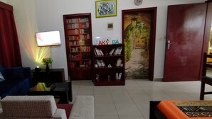 Uma sala de estar com um sofá azul, uma estante de livros, uma televisão e uma porta que dá para outro quarto.