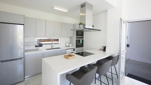 A modern kitchen with a central island, stainless steel appliances, and bar stools. - Protaras Olivine Villa Ol13 (Paralimni)