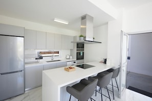 Una cocina moderna con una isla central, electrodomésticos de acero inoxidable y taburetes de bar.