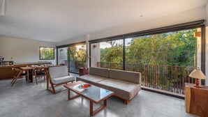 Amplia sala de estar con un ventanal, un sofá, una mesa de centro y una zona de comedor con sillas y una mesa.