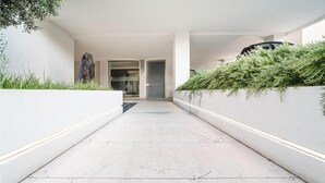 A modern hallway with a concrete floor, white walls, and a planter with green foliage on the right. - Stylish Residenza Torre Bianca 2 Bedroom Sleeps 6 (Lignano Sabbiadoro)