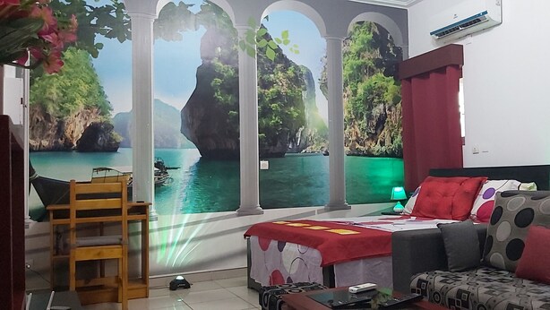 A bedroom with a bed, a sofa, a chair, a TV, and a large window with a scenic view. - Magnifique Studio Meuble (Abidjan)