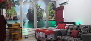 A bedroom with a bed, a sofa, a chair, a TV, and a large window with a scenic view. - Magnifique Studio Meuble (Abidjan)
