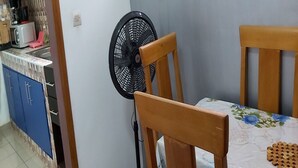 A dining area with a table, chairs, and a wall-mounted fan. - Magnifique Studio Meuble (Abidjan)