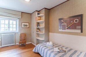 Un dormitorio con cama, una silla, una estantería, un radiador y una ventana.
