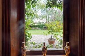A window with three ornate vases on a ledge, overlooking a garden with a potted tree and a stone pathway. - Villa Colle (Tremezzina)