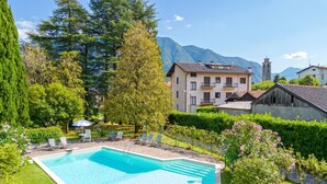 A swimming pool with lounge chairs, surrounded by greenery and a mountain backdrop. - Villa Colle (Tremezzina)