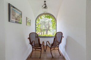 Una habitación con dos sillones de mimbre frente a un amplio ventanal con vistas a árboles y un edificio.