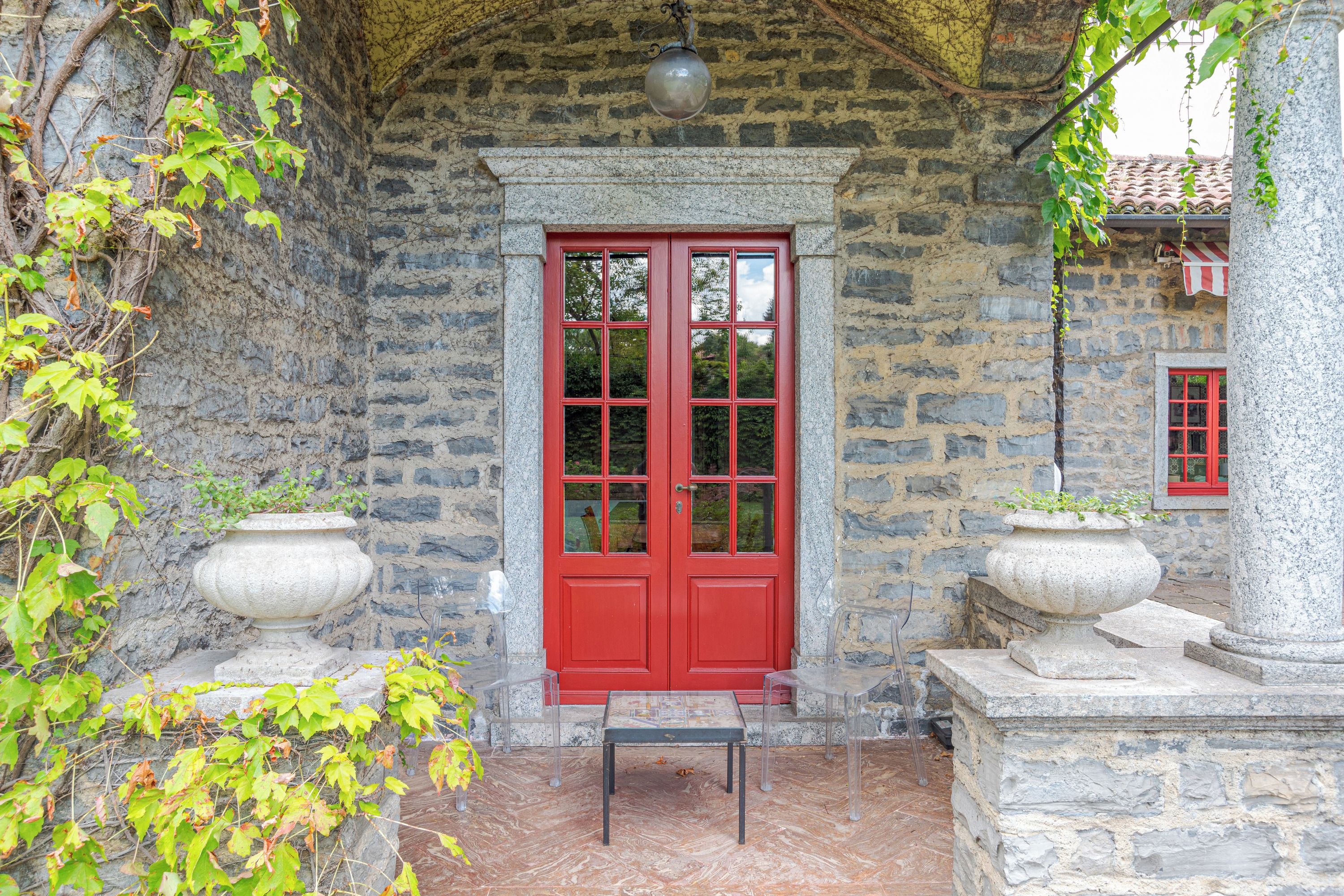 A stone building with a red door, two stone planters, and a small table.