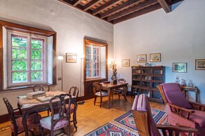 Una sala de estar acogedora con una mesa de madera, sillas, una estantería y un ventanal con vistas a la vegetación.