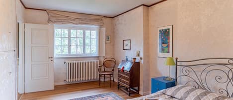 A bedroom with a bed, a dresser, a chair, a radiator, a window, and a painting on the wall.