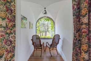 Habitación con dos sillas de mimbre orientadas a un amplio ventanal de arco con vistas a árboles y un jardín.