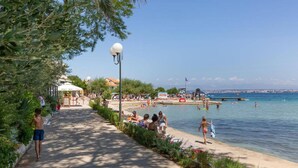 A coastal walkway with a beach, umbrellas, and people enjoying the seaside. - 3-bedroom Holiday House Giovanni (Preko)