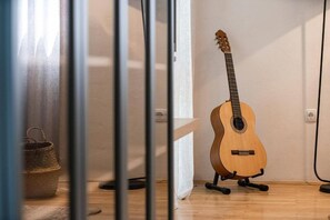 Une guitare posée sur un support dans une pièce dont le sol est en bois et un des murs est blanc.