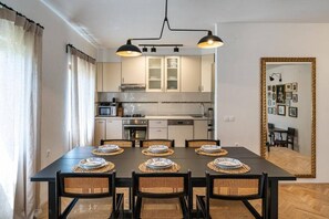 Uma área de refeições com mesa preta, seis cadeiras e pratos postos para uma refeição.