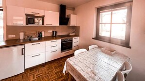 Cocina compacta con alacenas blancas, microondas, estufa y lavamanos. Hay una zona de comedor con mesa y sillas.