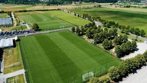Vista aérea de un gran campo deportivo rectangular con una valla, rodeado de árboles y edificios.