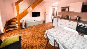 Cocina compacta con armarios blancos, microondas y horno. Una escalera de madera con barandilla de red desciende a un nivel inferior.