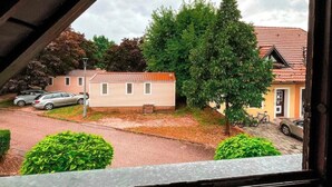 Vista desde una ventana sobre una zona residencial con una casa unifamiliar, un árbol y coches aparcados.