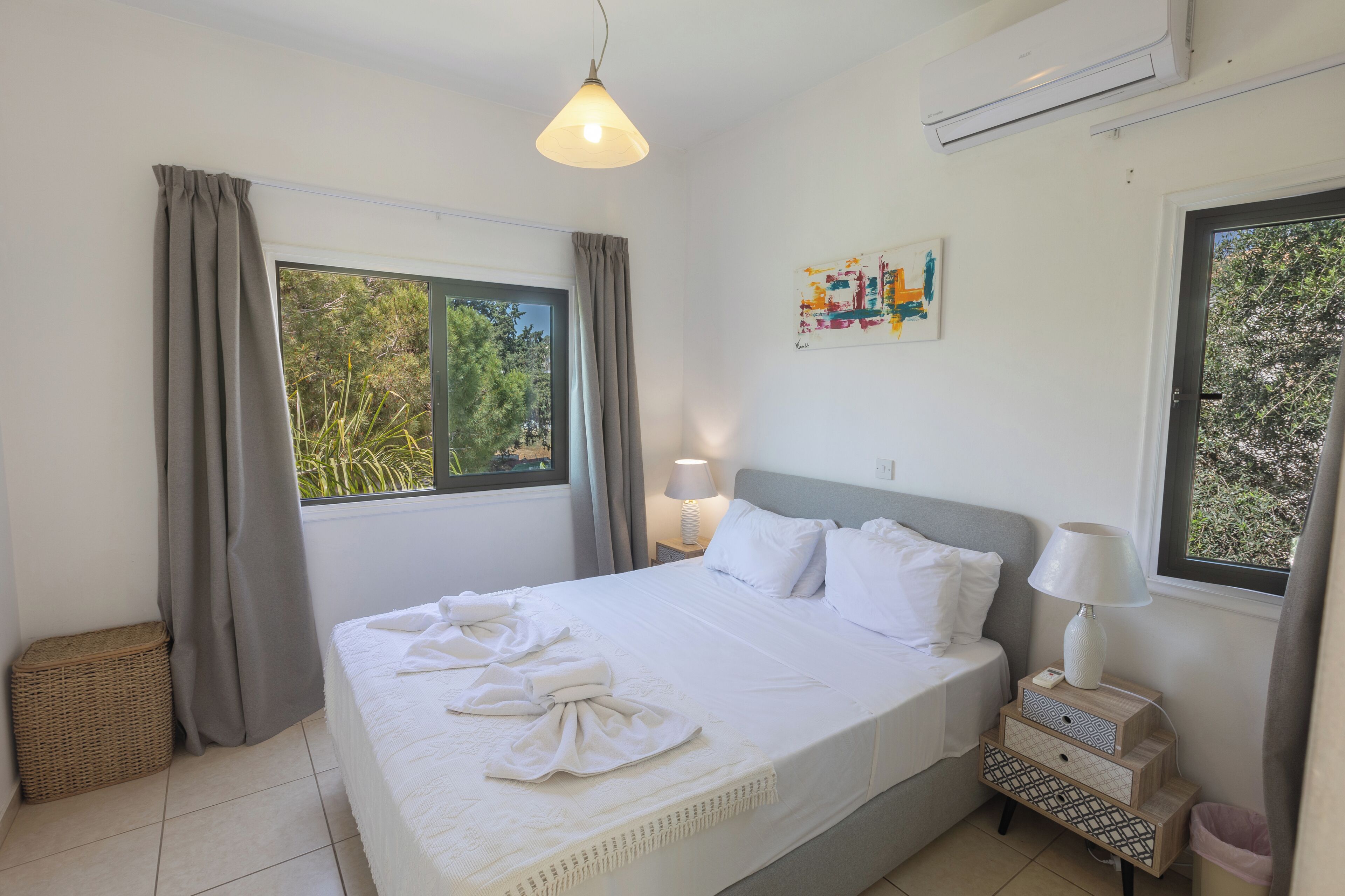 A neatly made bed with white linens and towels, a bedside lamp, and a small wooden nightstand with a lamp.