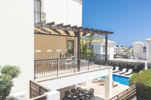 A balcony with a pergola, a pool area with lounge chairs, and a dining setup.
