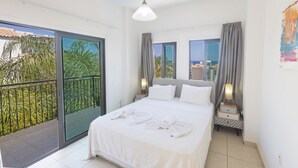 A modern hotel room with a large bed, two bedside tables with lamps, a balcony with a view of palm trees, and a sliding glass door. - Protaras Holiday Villa My5 (Paralimni)