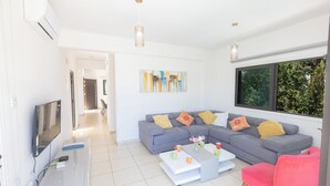 A modern living room with a grey sofa, a white coffee table, and a pink chair. There is a flat-screen TV on a white stand, and a painting on the wall. - Protaras Holiday Villa My5 (Paralimni)