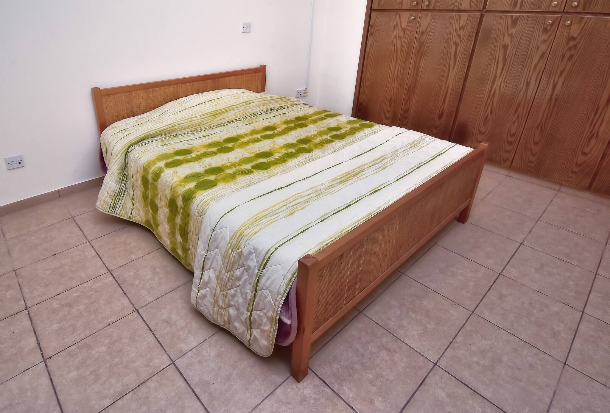 A bed in a room with a wooden headboard, a wardrobe, and tiled flooring.