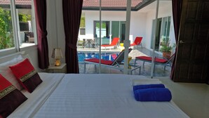 A hotel room with a bed, a view of a pool area, and a sliding glass door. - Phikun Private Pool Villa (Chalong)