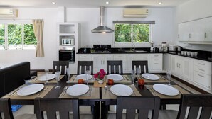 A modern kitchen with white cabinets, a central island, and a dining area set for six. - Phikun Private Pool Villa (Chalong)